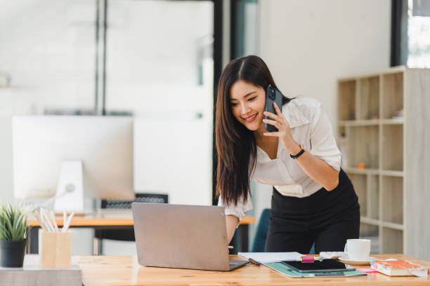 istock Busy professional businesswoman engages in a phone conversation while using laptop in a contemporary office workspace. 2150227279