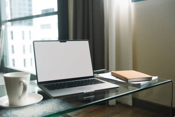 istock Laptop with white empty screen, notebook and coffee cup on glass table in living room. 2150236609