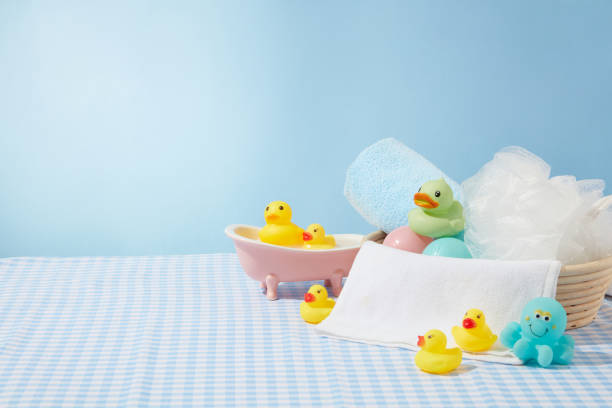 Baby bath products on table with plaid blue table cloth in bathroom, several rubber ducks, bath sponge over light blue background. Blank space for advertising, front view