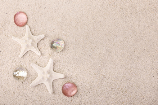Summertime textured background with white star fish and red glass pebbles on the white sand.