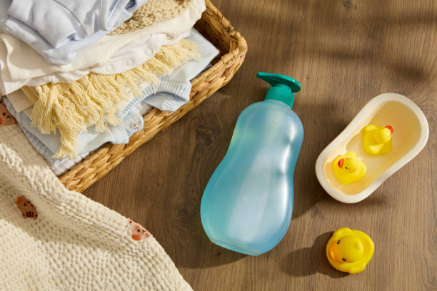 istock Baby care theme in rustic concept, a empty label blue bottle lay by a some rubber yellow ducks on wooden background, decorated by rattan basket of baby clothes. Space for advertising and copy space 2150247138