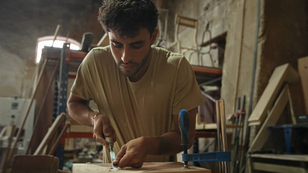 Young man carpenter carving wood block. Guy process timber bar. Male carpentry work skill. Joiner woodwork. Worker beat hammer. Person use chisel. Diy master class workshop Woodworker make job project