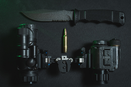 Tactical knife with a fixed blade, night vision binocular and 5.56x45mm cartridge. Close up photo