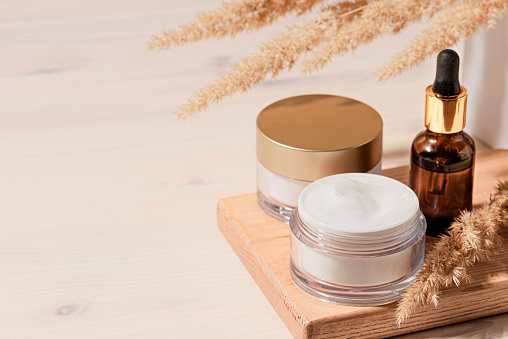 Cosmetic serum and beauty cream products with dry reeds or pampas grass on wooden beige background, trendy shot with hard shadows. Facial nourishing natural skin care, copy space.