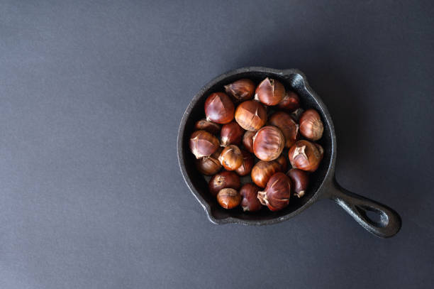 istock Roasted edible chestnuts in pan on dark gray neutral table background, flat lay with copy space. Traditional winter healthy treat 2150253420