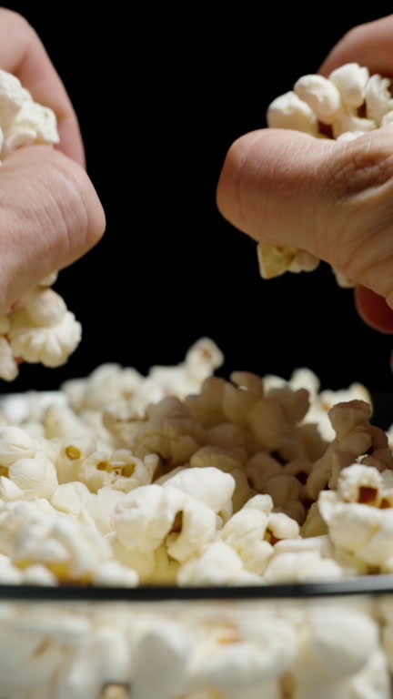 Vertical video. Two hands from both sides take a large handful of popcorn from the plate. Slow motion.