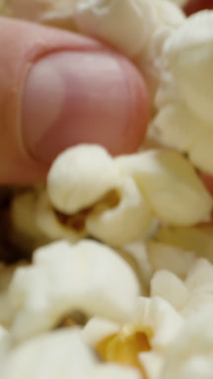 Vertical video. Close-up of hands taking handfuls of popcorn from both sides. Close-up.