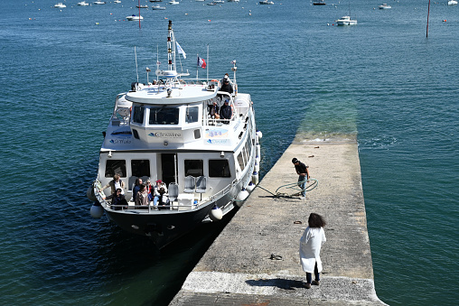 Dinard, France, april 18, 2024 : Corsaire shipping company boat between Saint-Malo and Dinard arriving at the disembarkation quay with a woman behind her waiting and a man tying the mooring line
