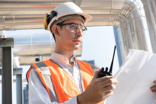istock Portrait Asia male engineer in protective workwear is performing a conducts system check with use paperwork and walkie talkie at rooftop building 2150255657