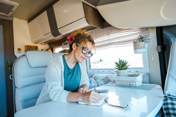 People living off grid traveling with camper van fulltimers vanlife. One woman writing notes inside a rv vehicle motorhome. Alternative home and lifestyle. Living off grid. Remote worker digital nomad personas que viven fuera de la red y viajan con furgonetas camper a tiempo completo. una mujer escribiendo notas dentro de una autocaravana. hogar y estilo de vida alternativos. vivir fuera de la red. nómada digital de trabajadores remotos