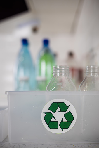 Vertical. Close-up of a green arrow recycling sign on a box of collected plastic bottles on a kitchen table. Concept of eco-friendly lifestyle and sorting plastic for recycling..