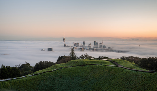 Auckland, New Zealand - August 31 2023: Auckland skyline and Sky Tower above the sea of fog at dawn. View from Mount Eden summit with the volcanic crater in foreground.