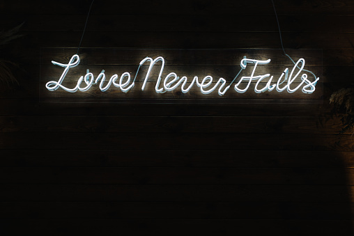 Love never fails. Text Corinthians 13 Holy bible. An Inspirational motivating wise quote from Corinthians. Text with neon light on wooden wall background.
