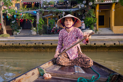 Vietnamese women in a row boat, old town in Hoi An city, Vietnam. Hoi An is situated on the east coast of Vietnam. Its old town is a UNESCO World Heritage Site because of its historical buildings.