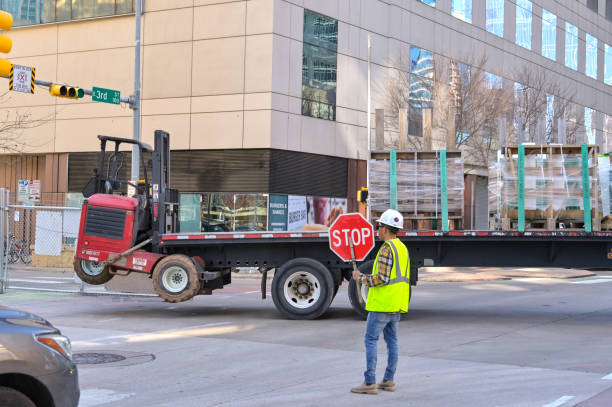Austin, Texas, USA - 8 February 2023: Construction worker holding up a stop sign to halt traffic while a large articulated truck reverses into a building site