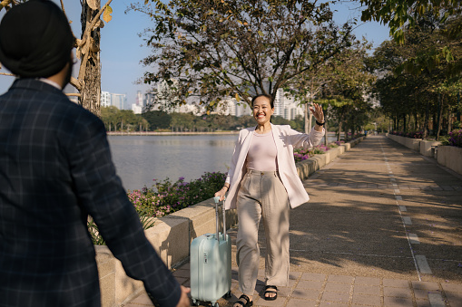 Happy female entrepreneur walking towards her colleague after arriving from a business trip in the park.