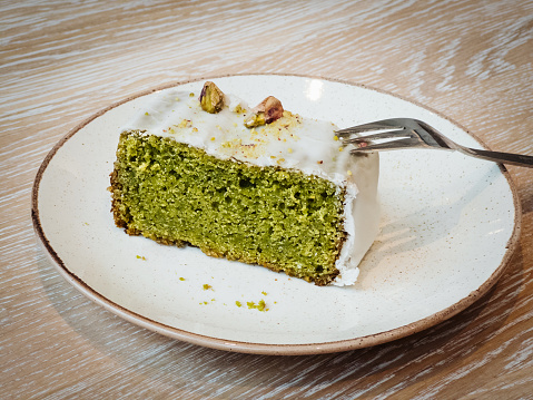 Pistachio cake, green, juicy, delicious with icing. Vegan with lime. Trend on a round plate on a rustic wooden table. Bright picture