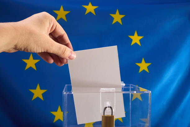 istock Hand placing a voting ballot into a clear box with EU flag backdrop 2150265090