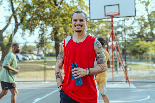 Diverse male friends standing on a basketball court and holding water bottle