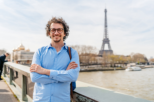 Portrait of a handsome young man standing on the bridge in Paris in France. View of the Eiffel Tower in the distance.