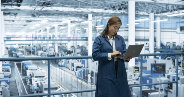 istock Electronics Manufacturing Technician Working on a Laptop Computer at a Factory Space. Asian Female Specialist Developing, Maintaining, Fine-Tuning Programs for Machine Production and Assembly 2150271073