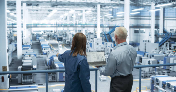 istock Experienced Male and Female Engineers Standing on a Platform, Using Laptop Computer and Discussing Production at a Modern Automated Electronics Manufacture with AI Support 2150271257