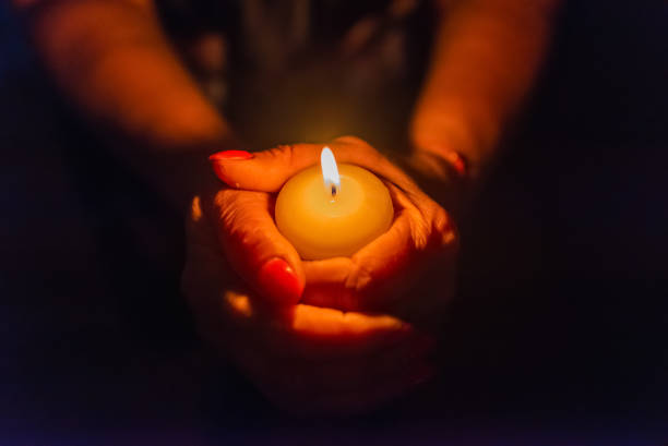 istock Candle in female hands on black dark background.Prayers candle in hands. 2150271382