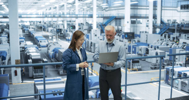 istock Factory Managers Working on Laptop at a Modern Manufacture with Autonomous Robot Hands. Female and Male Specialists Monitoring Technical Data on a Computer, Analyzing Reports and Planning Updates 2150271467