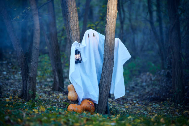 Carefree woman pretending to be a ghost during Halloween in the forest.