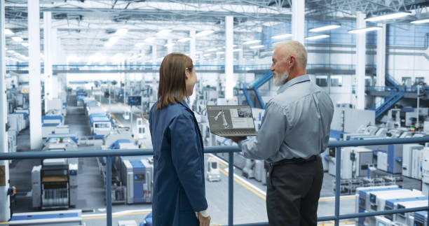 istock Middle Aged Engineer and Young Japanese Technician Having a Conversation and Using Laptop Computer. Specialists Monitoring, Analyzing Conditions at a Modern Electronics Factory with Automated Robots 2150271705