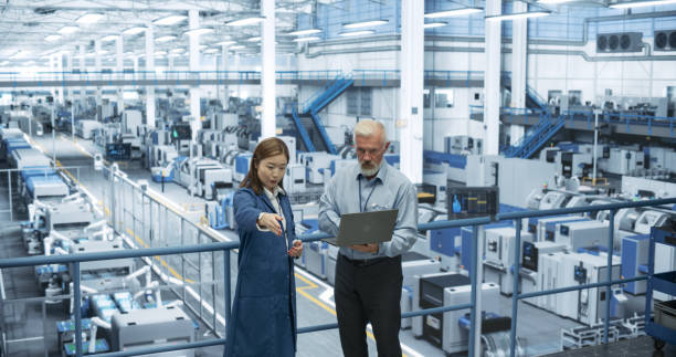 istock Middle Aged Engineer and Young Japanese Technician Having a Conversation and Using Laptop Computer. Specialists Monitoring, Analyzing Conditions at a Modern Electronics Factory with Automated Robots 2150271708