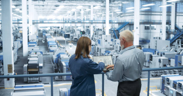 istock Portrait of a Middle Aged Engineer and Happy Asian Scientist Using Laptop Computer and Talking in a Factory Facility with Equipment Producing Modern Electronic Components for Different Industries 2150271808