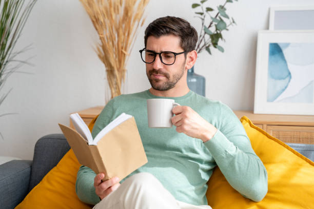 istock Relaxed man enjoying book and coffee on sofa 2150275122