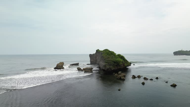 4k Video Footage - Aerial view of a rocky headland beach with crashing waves during the day. Cape with cliffs by the sea and green plants on it at tropical island in Gunungkidul, Yogyakarta, Indonesia