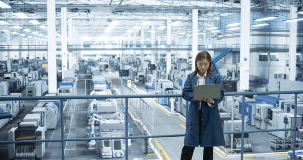 istock Experienced Female Engineer Standing on a Platform, Using Laptop to Monitor Data on a Computer, Check Reports and Plan a Research Strategy. Empowered Factory Manager at Work 2150275967