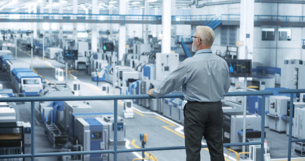 istock Industrial Engineer Working at a Technology Factory. Middle Aged Manager Standing on a Platform at Work, Looking at the Production Manufacturing Complex. Automated Robots Moving Around the Hall 2150276122