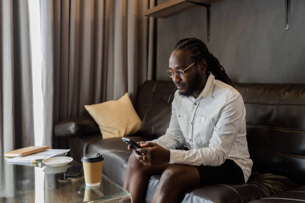 istock Young African American man relaxing on soft at home, texting messaging on smartphone. man using mobile phone chatting online message, shopping online from home 2150276660