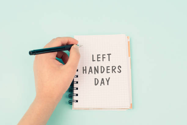 istock Left handers day is standing on a notebook, writing with the left hand, pen and table 2150276840