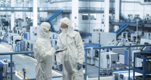 istock Two Female Technicians in Protective Coveralls Having a Conversation and Using Tablet Computer. Specialists Monitoring, Analyzing Conditions at a Modern Electronics Factory with Automated Robots 2150276863