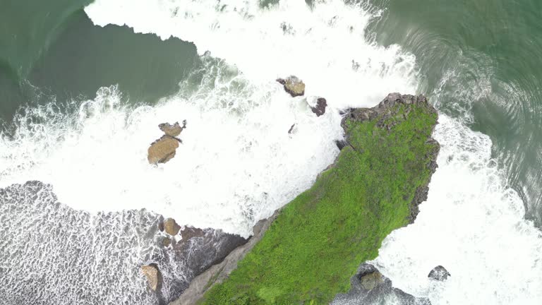 4k Video Footage - Aerial view of a rocky headland beach with crashing waves during the day. Cape with cliffs by the sea and green plants on it at tropical island in Gunungkidul, Yogyakarta, Indonesia