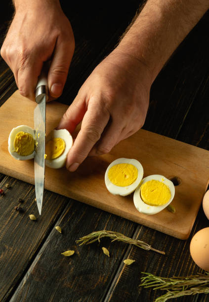 istock Chef cuts a boiled egg with a knife before preparing an eggs dish. Low key calorie diet concept on kitchen table. Place for advertising 2150281750