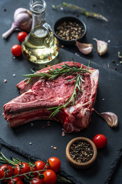 istock Raw beef steak on the bone on the black slate serving plate, decorated with ingredients: cooking oil, dry pepper, cherry tomatoes and herbs. 2150281872