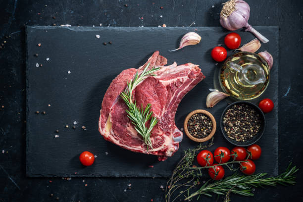 istock Raw beef steak on the bone on the black slate serving plate, decorated with ingredients: cooking oil, dry pepper, cherry tomatoes and herbs. 2150281949