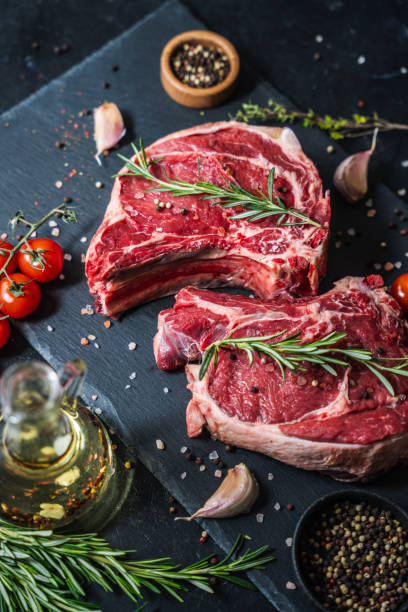 istock Two raw beef steaks on the bone on a black slate serving plate, decorated with ingredients and spices. 2150282051