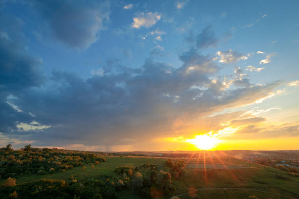 Optimistic summer scenery. The majestic sunset scene with approaching rainy clouds with falling rain over green summer hills. Beautiful sunset sky with clouds and sunshine. Summer nature background.
