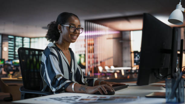 istock Black Woman Working on Desktop Computer in Creative Office. African American Marketing Manager Writing Email Messages, Developing Social Media Strategy, and Researching Project Plan Details Online 2150285021