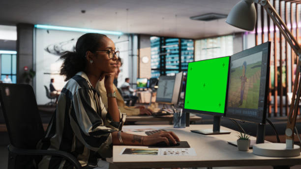 istock Female Black Game Designer Using Desktop Computer With Green Screen Chromakey on Display, Designing Characters In 3D Modeling Software For Survival Video Game. Woman Working In Game Development Office 2150285870