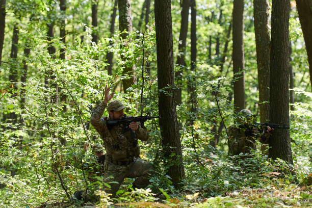 An elite soldier, camouflaged and stealthily navigating through dangerous woodland terrain, executes a covert mission in a secluded forest area An elite soldier, camouflaged and stealthily navigating through dangerous woodland terrain, executes a covert mission in a secluded forest area. militant groups stock pictures, royalty-free photos & images