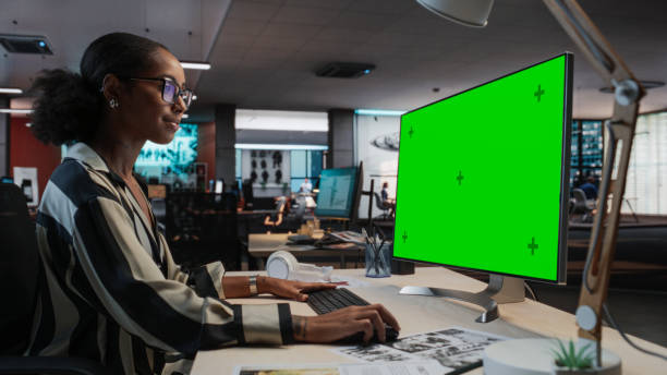 istock Portrait of Creative Black Female Sitting at a Desk Using Desktop Computer with Mock-up Green Screen. Female Concept Artist Working in Game Design Startup Office, Creating Immersive Gameplay. 2150286649