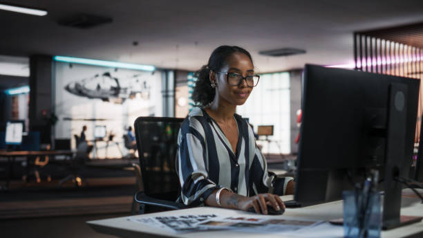 istock Young Black Woman Working on Desktop Computer in Creative Office. Multiethnic Marketing Manager Writing Email Messages, Developing Social Media Strategy, and Researching Project Plan Details Online 2150286702